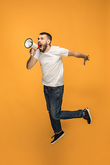 Image showing Jumping fan on orange background. The young man as soccer football fan with megaphone