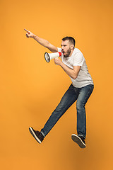 Image showing Jumping fan on orange background. The young man as soccer football fan with megaphone