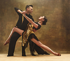 Image showing Dance ballroom couple in gold dress dancing on studio background.