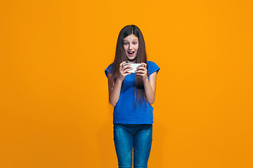 Image showing The happy teen girl standing and smiling against orange background.