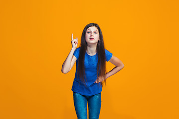 Image showing Beautiful female half-length portrait on orange studio backgroud. The young emotional teen girl