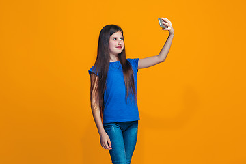 Image showing The happy teen girl standing and smiling against orange background.