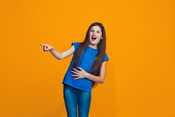 Image showing The happy teen girl standing and smiling against orange background.