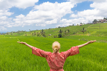 Image showing Relaxed fashionable caucasian woman wearing red asian style kimono, arms rised to sky, enjoying pure nature of beautiful green rice fields on Bali.