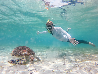 Image showing Woman on vacations wearing snokeling mask swimming with sea turtle in turquoise blue water of Gili islands, Indonesia. Underwater photo.