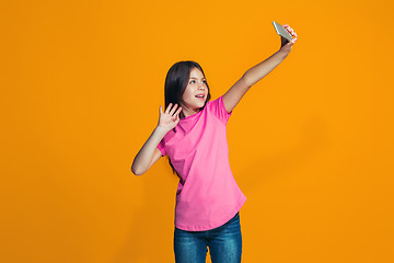 Image showing The happy teen girl standing and smiling against orange background.