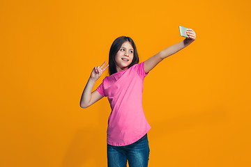 Image showing The happy teen girl standing and smiling against orange background.