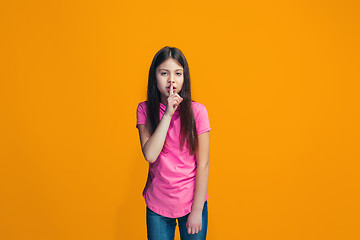 Image showing The young teen girl whispering a secret behind her hand over orange background