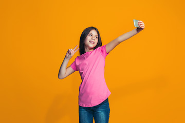 Image showing The happy teen girl standing and smiling against orange background.