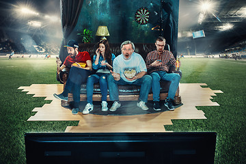 Image showing Soccer football fans sitting on the sofa and watching TV in the middle of a football field.