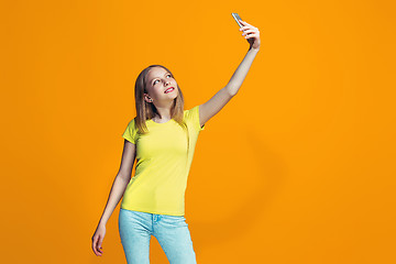 Image showing The happy teen girl standing and smiling against orange background.