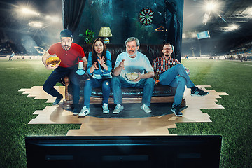 Image showing Soccer football fans sitting on the sofa and watching TV in the middle of a football field.