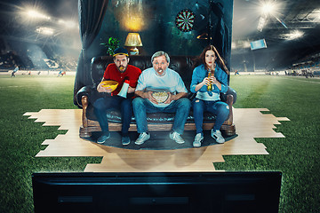 Image showing Soccer football fans sitting on the sofa and watching TV in the middle of a football field.