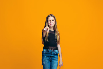 Image showing The happy teen girl pointing to you, half length closeup portrait on orange background.