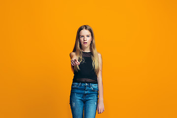 Image showing The happy teen girl pointing to you, half length closeup portrait on orange background.