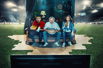 Image showing Soccer football fans sitting on the sofa and watching TV in the middle of a football field.