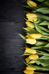 Image showing Beautiful yellow tulips on black rustic wooden background. Top view