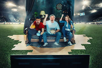 Image showing Soccer football fans sitting on the sofa and watching TV in the middle of a football field.