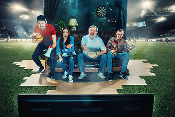 Image showing Soccer football fans sitting on the sofa and watching TV in the middle of a football field.