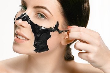 Image showing Young beautiful woman applying a mask for the face of the therapeutic black mud. Spa treatment