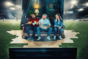 Image showing Soccer football fans sitting on the sofa and watching TV in the middle of a football field.