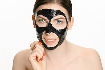 Image showing Young beautiful woman applying a mask for the face of the therapeutic black mud. Spa treatment