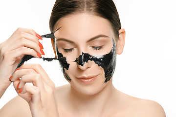 Image showing Young beautiful woman applying a mask for the face of the therapeutic black mud. Spa treatment