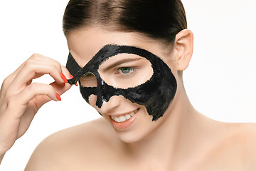 Image showing Young beautiful woman applying a mask for the face of the therapeutic black mud. Spa treatment