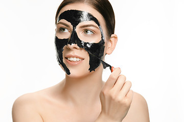 Image showing Young beautiful woman applying a mask for the face of the therapeutic black mud. Spa treatment