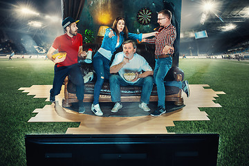 Image showing Soccer football fans sitting on the sofa and watching TV in the middle of a football field.