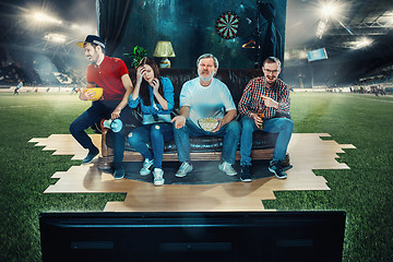 Image showing Soccer football fans sitting on the sofa and watching TV in the middle of a football field.