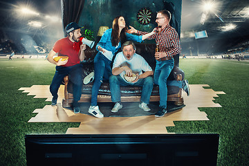 Image showing Soccer football fans sitting on the sofa and watching TV in the middle of a football field.