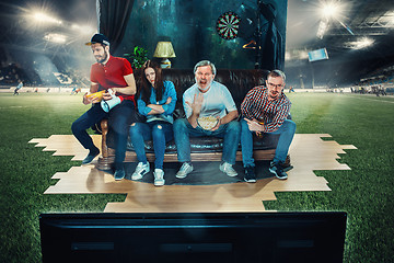 Image showing Soccer football fans sitting on the sofa and watching TV in the middle of a football field.