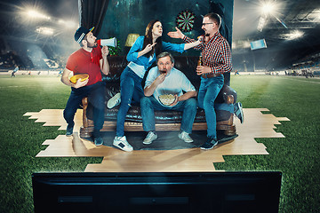 Image showing Soccer football fans sitting on the sofa and watching TV in the middle of a football field.