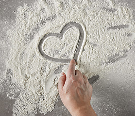 Image showing cook hand drawing heart shape in flour