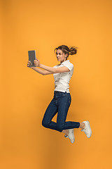 Image showing Image of young woman over orange background using laptop computer or tablet gadget while jumping.