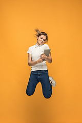 Image showing Image of young woman over orange background using laptop computer or tablet gadget while jumping.