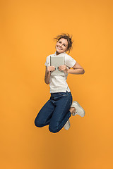 Image showing Image of young woman over orange background using laptop computer or tablet gadget while jumping.