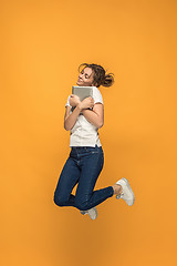 Image showing Image of young woman over orange background using laptop computer or tablet gadget while jumping.