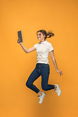 Image showing Image of young woman over orange background using laptop computer or tablet gadget while jumping.