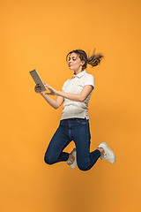 Image showing Image of young woman over orange background using laptop computer or tablet gadget while jumping.