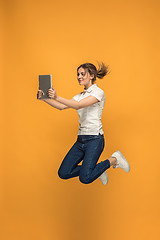 Image showing Image of young woman over orange background using laptop computer or tablet gadget while jumping.