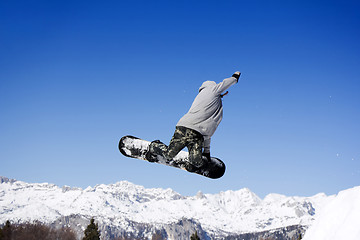 Image showing Extreme Jumping Snowboarder at jump above mountains at sunny day