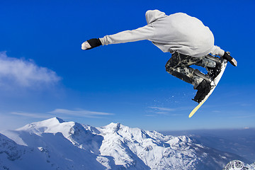 Image showing Extreme Jumping Snowboarder at jump above mountains at sunny day