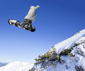 Image showing Extreme Jumping Snowboarder at jump above mountains at sunny day