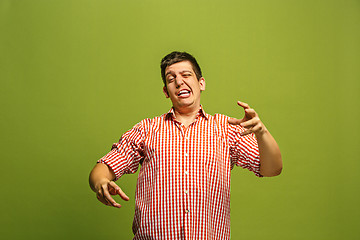 Image showing Beautiful male half-length portrait isolated on green studio backgroud. The young emotional surprised man