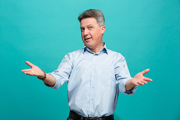 Image showing Beautiful male half-length portrait isolated on blue studio backgroud. The senior emotional surprised man