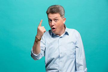 Image showing Beautiful male half-length portrait isolated on blue studio backgroud. The senior emotional surprised man