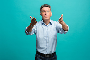 Image showing Beautiful male half-length portrait isolated on blue studio backgroud. The senior emotional surprised man