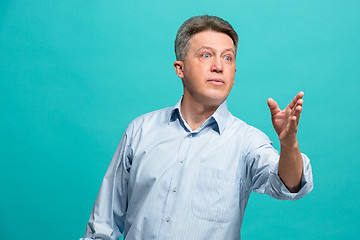 Image showing Beautiful male half-length portrait isolated on blue studio backgroud. The senior emotional surprised man